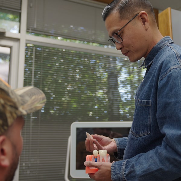 Dentist is holding dental implant model and smiling