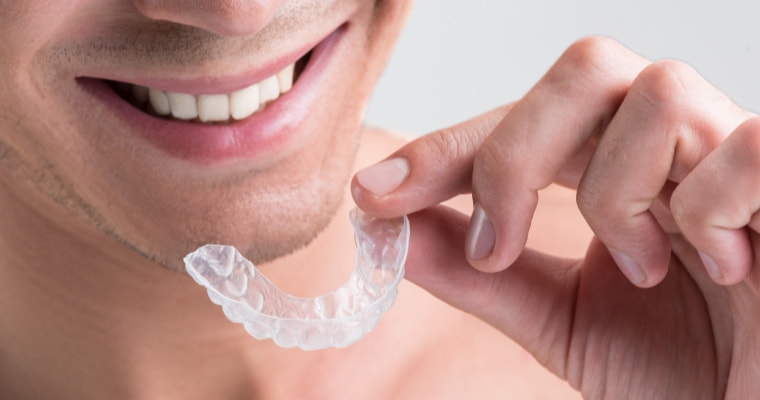 A close-up of a man holding a clear aligner tray